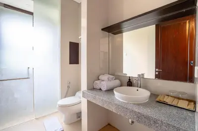 a bathroom with a sink and a toilet and a mirror at D'Maya Villa Jimbaran By Island Escape in Jimbaran