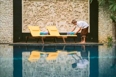 a man sitting on a bench next to a swimming pool at Ghania Peaceful 3 BR Private Pool Villa in Jimbaran