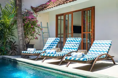 a group of four chairs sitting next to a swimming pool at Villa Merah in Seminyak