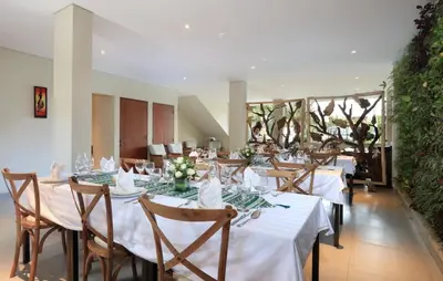 a dining room with white tables and chairs and plants at Desa Di Bali Villas in Kerobokan