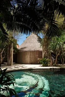 a swimming pool in front of a thatched building at The Island Houses Seminyak in Seminyak