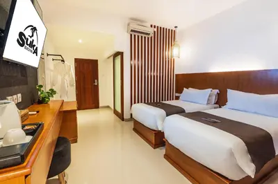 a hotel room with two beds and a desk at Suka Beach Inn in Kuta