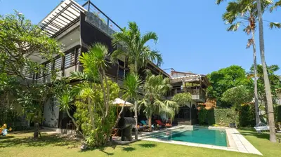 an exterior view of a house with a swimming pool and palm trees at NicoNico Mansion by Villa Finder in Seminyak