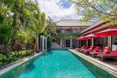 a pool with chairs and umbrellas next to a house at The Residence Seminyak in Seminyak
