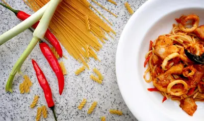 a plate of pasta and peppers on a table at Away Bali Legian Camakila in Legian