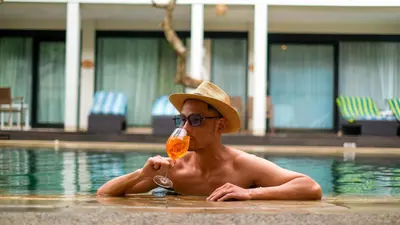 a man in a swimming pool drinking a drink at Away Bali Legian Camakila in Legian