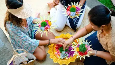 two women sitting on the ground with flowers on a plate at Away Bali Legian Camakila in Legian