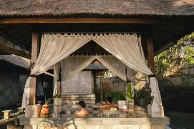 two people are sitting under a curtain in a pavilion at Jimbaran Puri, A Belmond Hotel, Bali in Jimbaran