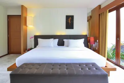 a bedroom with a large white bed with a bench at Abi Bali Resort and Villa in Jimbaran