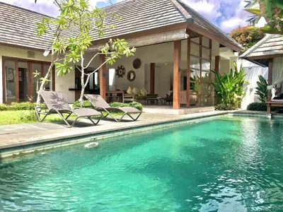 a swimming pool with two chairs in front of a house at Villa Kim Seminyak in Seminyak