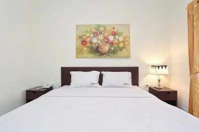 a bedroom with a white bed and a painting on the wall at RedDoorz at Benesari 2 Legian in Kuta