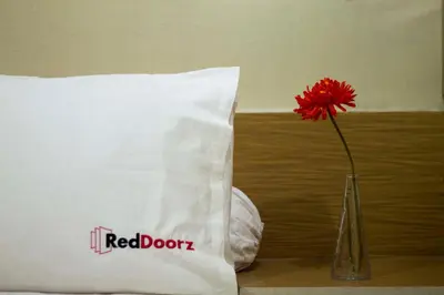 a red flower in a vase next to a pillow at RedDoorz at Benesari 2 Legian in Kuta