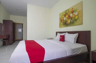 a bedroom with a large bed with a painting on the wall at RedDoorz at Benesari 2 Legian in Kuta