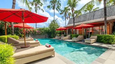 a pool with chairs and umbrellas next to a building at Villa Taramille by Villa Finder in Kerobokan