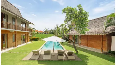 a pool with chairs and an umbrella next to a house at Villa Alea by Villa Finder in Kerobokan