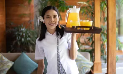 a woman holding a tray of orange juice at Villa Little Mannao by Villa Finder in Kerobokan