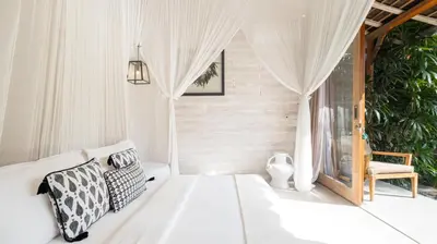 a white bedroom with a bed and a chair at Villa Little Mannao by Villa Finder in Kerobokan