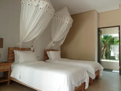 two beds in a bedroom with white sheets and a window at La Dolce Villa in Seminyak