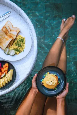 a person holding a plate of food in a pool at Villa Du Bah - Cozy Tropical 3BR Villa 12min To Beach in Kerobokan