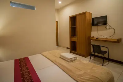a bedroom with a bed with a tv and a chair at Kuta Suci Guesthouse in Kuta