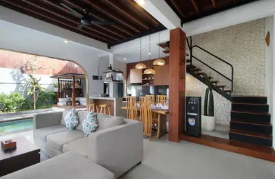 a living room with a couch and a kitchen and a staircase at Sudha Villa Bali Anyelir in Seminyak