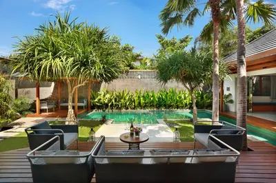 a patio with chairs and a pool with palm trees at Villa Odyssey in Seminyak