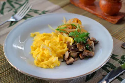 a white plate of food with scrambled eggs and mushrooms at Sleepwell Seminyak in Seminyak