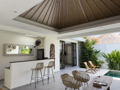 a patio with a bar and chairs and a swimming pool at Aster Villa Seminyak in Seminyak