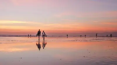 a group of people walking on the beach with surfboards at Swiss-Belexpress Kuta Legian in Kuta