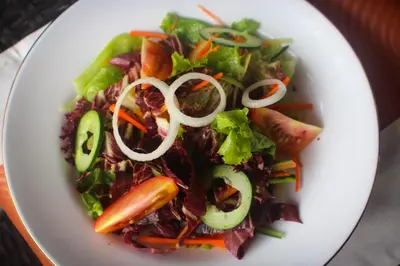 a white plate with a salad with vegetables on it at The Diana Suite in Kuta