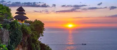 a sunset over the ocean with a building on a cliff at Flora Apartment Bali in Seminyak