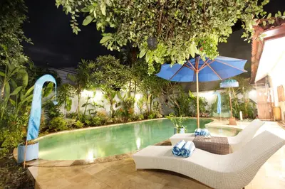 a swimming pool with chairs and an umbrella at Villa Alam Biru Gardenia in Seminyak