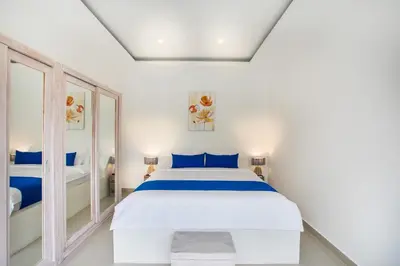 a white bedroom with a bed and a mirror at Holyfat Villa in Seminyak