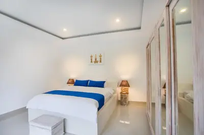 a white bedroom with a bed and a mirror at Holyfat Villa in Seminyak