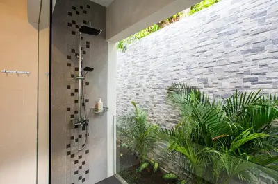 a bathroom with a walk in shower next to a stone wall at Villa Kamboja Deluxe in Seminyak