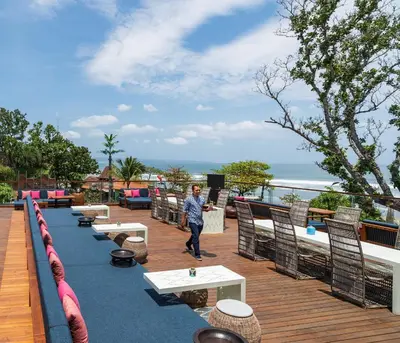 a man walking on a deck with tables and chairs at Hotel Indigo Bali Seminyak Beach by IHG in Seminyak