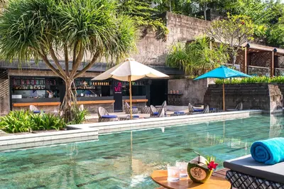 a pool with chairs and umbrellas and a bar at Hotel Indigo Bali Seminyak Beach by IHG in Seminyak