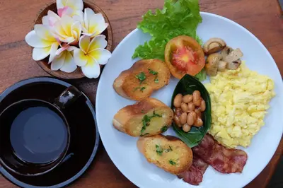 a plate of breakfast food with eggs bacon and mushrooms at D'Pande Kuta in Kuta