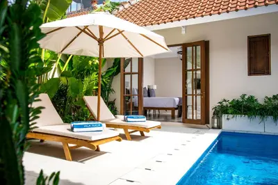 a patio with two chairs and an umbrella next to a pool at Villa Tsuchi in Seminyak