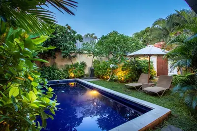 a swimming pool in a garden with two chairs and an umbrella at Villa Rani 3 in Seminyak