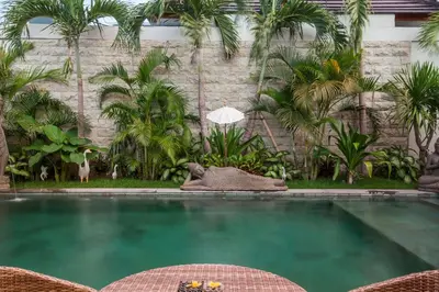 a swimming pool with two chairs and palm trees at Ambermoon Villas in Seminyak