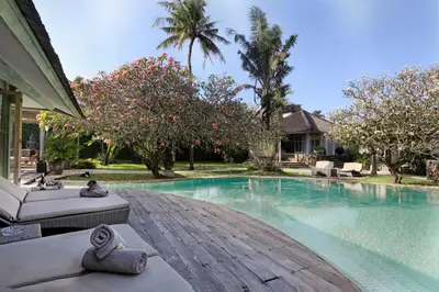 a swimming pool with a wooden deck next to a house at Maya Villa - Seminyak in Seminyak