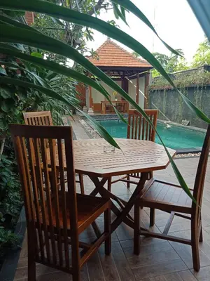 a wooden table and chairs next to a pool at D'puja Home Stay and Spa in Nusa Dua