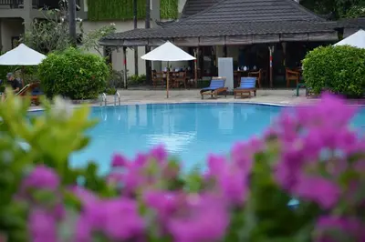 a swimming pool with chairs and umbrellas and purple flowers at Sofi Apartment at Jayakarta Residence in Legian