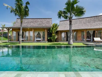 a swimming pool in front of a house with palm trees at Mannao Estate by Villa Finder in Kerobokan