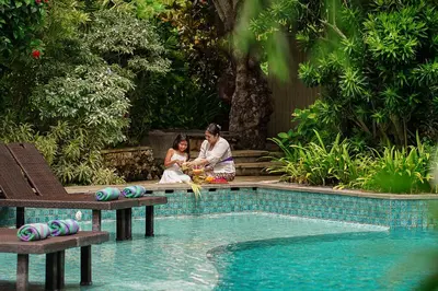 a man and a woman sitting next to a swimming pool at Royal Tulip Springhill Resort Jimbaran in Jimbaran