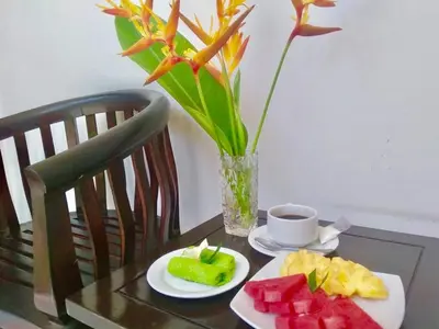 a table with a plate of fruit and a vase with flowers at The Celuk Homestay in Jimbaran