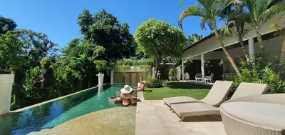 a woman in a hat sitting next to a swimming pool at Villa Anema Umalas in Seminyak