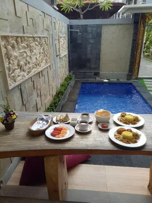 a table with plates of food on it with a swimming pool at The Surya Kuta Villa in Kuta