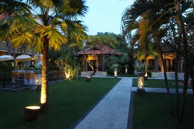 a courtyard with palm trees and a building with lights at Adhi Jaya Hotel in Kuta